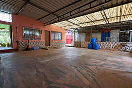 A void covered occasion space with a tiled floor and open sides, showing a perspective on the garden outside, at Khelaghar Baganbari.