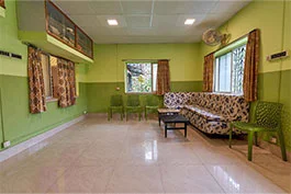 A splendid room with green walls and a designed couch, with green seats and a dark foot stool on a white tiled floor, offering an open to sitting region at Khelaghar Baganbari.